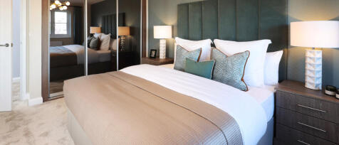 Modern bedroom with a large bed, decorative cushions, bedside lamps, and mirrored wardrobe doors at