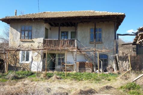 Front facade of an old Bulgarian house showing wooden balcony, windows, and garden space