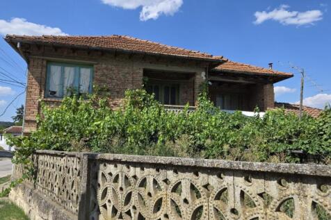 Front view of a brick house with green framed windows and grapevines growing along a decorative concrete fence