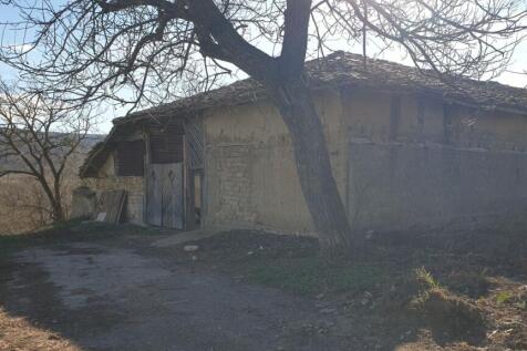 View of a large rustic outbuilding featuring wooden doors and mud brick walls, surrounded by bare trees
