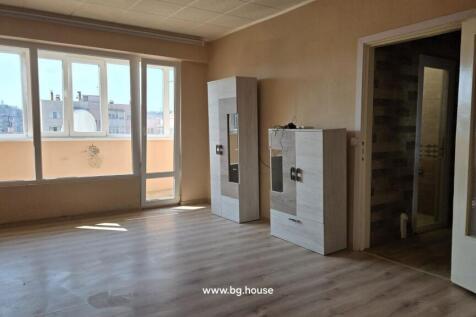 Spacious living room featuring large windows and a door leading to the balcony, with light wood flooring and two light-colored storage cabinets against the wall.