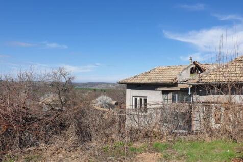 View of the house rear showing the tiled roof, bare trees, and dry vines on a wire fence