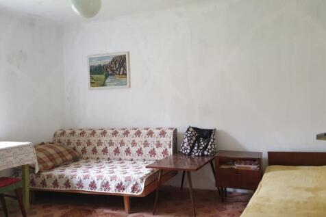 Interior room showing a window, table, chairs, a sofa, and a single bed with a yellow blanket.