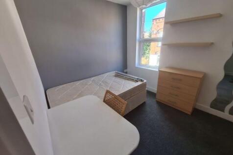 A cozy, well-lit single bedroom featuring a bed...