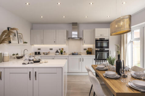 A modern white kitchen with a breakfast bar and dining area is illuminated by recessed lighting and