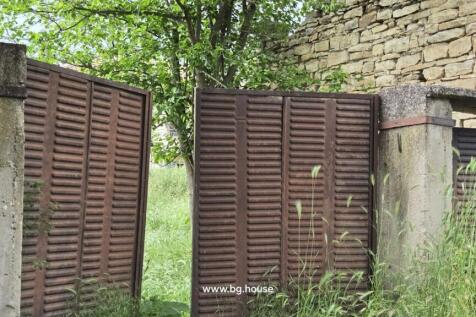 Close-up of a rusty metal gate next to a stone wall with green plants growing around it.