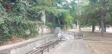Paved outdoor seating area featuring stone benches along an ivy-covered stone wall surrounded by trees.