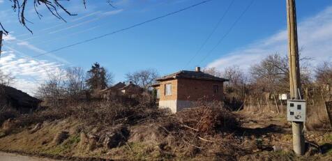 Brick house with tiled roof seen behind an electrical pole and surrounded by dry bushes and rural landscape.