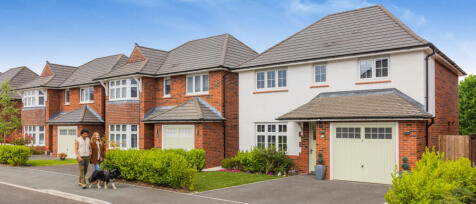 Modern red brick and white detached houses with driveways and greenery under a blue sky in woodland