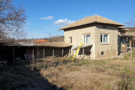 Exterior view of a traditional Bulgarian house with a tiled roof and adjacent outbuildings in a rural yard