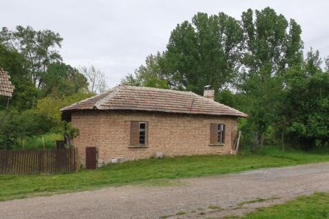 View of the small brick house with tiled roof and wooden shutters surrounded by greenery