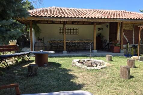 Garden space featuring a circular fire pit surrounded by benches and a covered patio with a dining table and chairs.