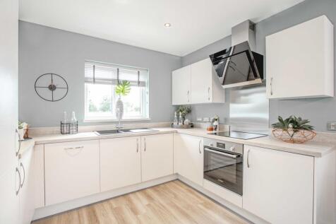 A modern white kitchen with a light wood floor in the foreground and a light gray wall with a window