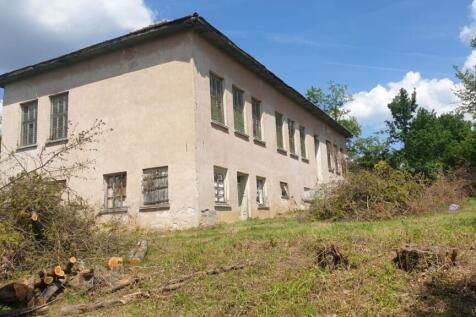 View of the two-story old school building with barred windows and a grassy yard with trimmed bushes