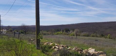 View of a grassy rural field bordered by a stone wall and a utility pole, with hills in the background under a partly cloudy sky.