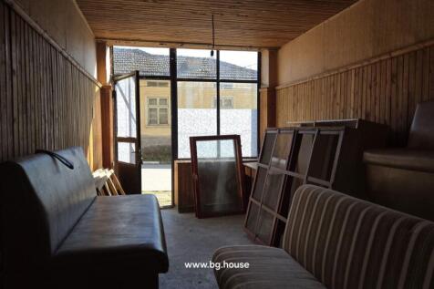 Room with wooden panel walls containing two sofas, window frames, and various stored items.