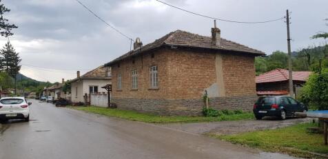 Exterior corner view of a brick house with tiled roof located on a village street with parked cars and neighboring houses.