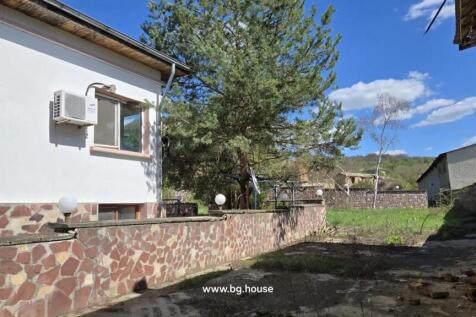Stone paved yard area adjacent to a white building, bordered by a stone wall and trees.