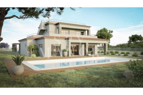 Heated swimming pool and lawn area outside a luxury detached villa in Vale del Rei, Algarve, showing the modern two-storey facade with double-glazed glass doors.
