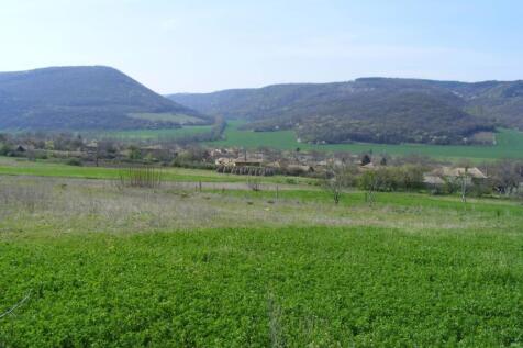 View of green fields and a village with forested hills in the distance under a clear sky