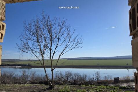 Lake and countryside view with a leafless tree visible through an opening in the unfinished brick walls.