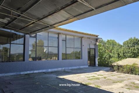 Covered terrace area with large windows and metal door, surrounded by trees and greenery