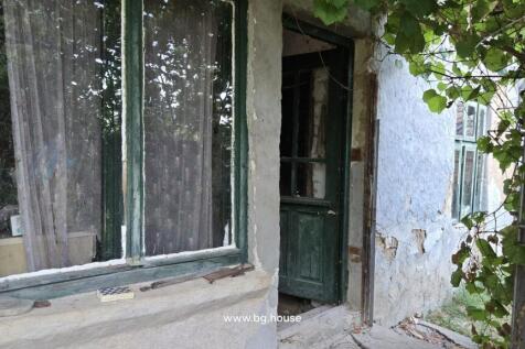 View of the house entrance showing a green wooden door and window with lace curtains on a textured plaster wall.