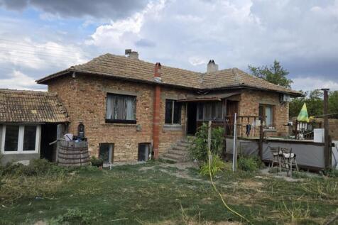 Exterior view of a brick house with a tiled roof, wooden porch, and garden area with grass and plants.