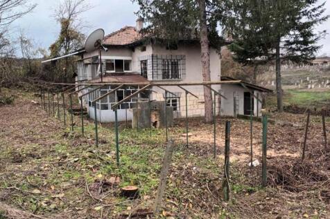 View of the two-storey house with a tiled roof, enclosed porch, and garden space with trees and fencing