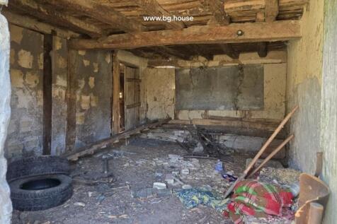 Inside a rustic room featuring wooden ceiling beams, scattered debris, old tires, and colorful blankets on the floor.