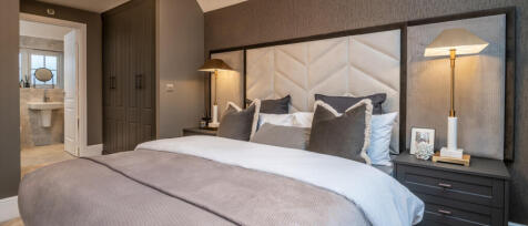 Modern bedroom with a large bed, stylish headboard, bedside lamps, and a view into an en-suite bathr