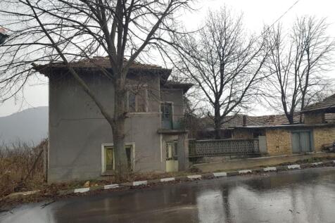 Side perspective of the two-storey house with visible balcony and bare trees on a rainy day