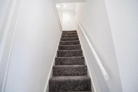 Carpeted internal staircase with a white handra...
