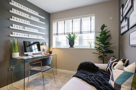 A modern home office with a glass desk and computer in the foreground is complemented by a window wi