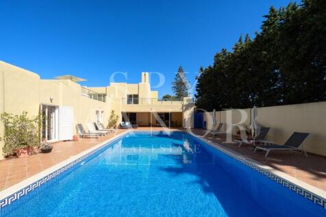 Large swimming pool with sun terraces and sunbeds at a Moorish villa for sale in Carvoeiro Clube, Algarve, under a blue sky.