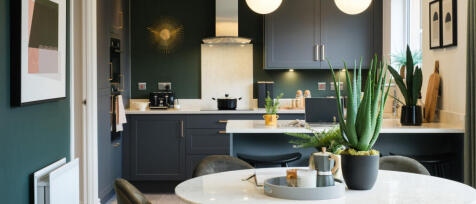 Modern kitchen with dark green cabinets, a marble breakfast bar, and various potted plants on the wi