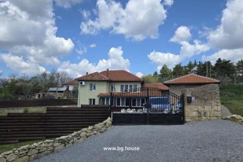 View of house behind black metal gate with gravel driveway and wooden fence on the side