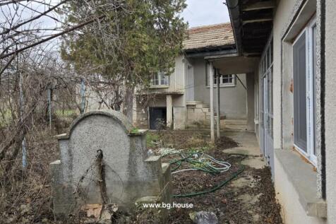 View of the corner house exterior showing a stone water fountain, garden hose, and entrance steps.