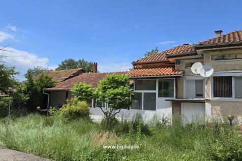 Side perspective of the Bulgarian house showing tiled roof, enclosed garden with tall grass and small trees.