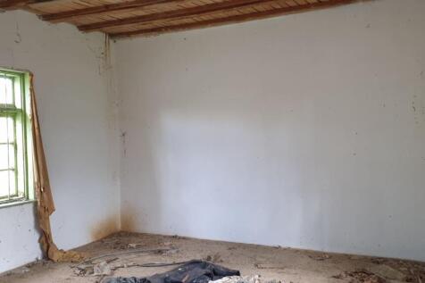 Interior room showing white walls, green door frames, and a floor covered with debris and dirt.