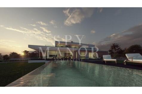 Algarve luxury villa for sale in Carvoeiro, showcasing two-story contemporary architecture, floor-to-ceiling glass walls, a private swimming pool, sun loungers, and expansive lawns.