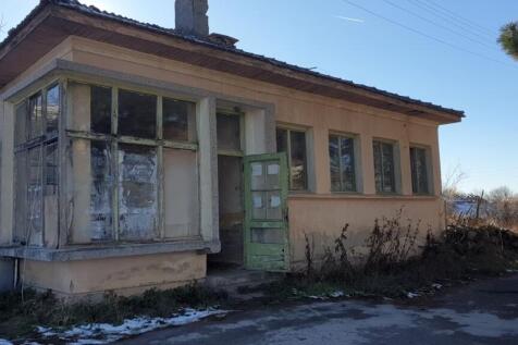 Exterior view of an old Bulgarian bakery building with multiple windows and a green wooden door open to the outside.