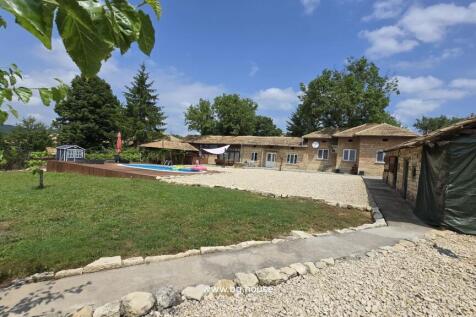 Outdoor view showing the Bulgarian house, swimming pool, garden, and surrounding trees under a partly cloudy sky.