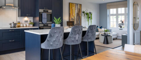 Modern open-plan kitchen and living room with navy cabinetry, grey barstools, and bright windows in