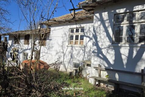 Side facade of the white cottage showing several windows and a wooden bench beside an overgrown garden area.
