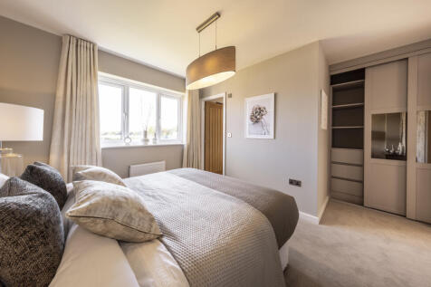 A cozy bedroom features a neatly made bed with plush grey pillows in the foreground and a neutral-to