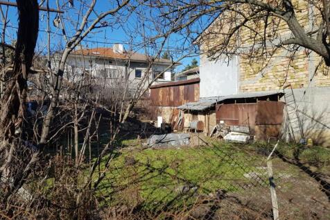 Grassy building land featuring garden beds covered with plastic and surrounding residential buildings