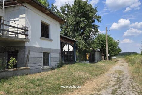 Side view of a white two-storey house with wooden shutters and fenced garden next to a rural dirt road