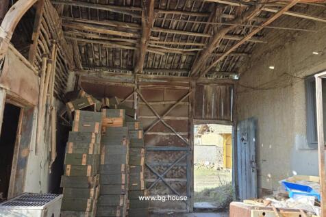 Interior of a covered storage area featuring stacked wooden crates, a large metal door, and an open wooden door leading outside.