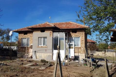 Side view of a small brick house with tiled roof and enclosed porch, dry garden and fencing